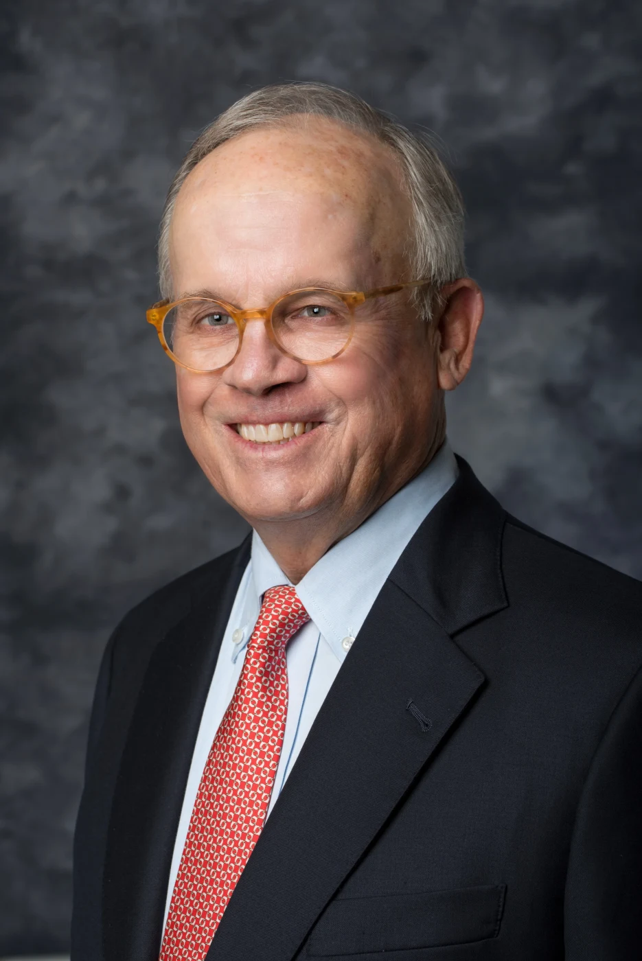 Classic executive portrait of a smiling man in glasses and red tie