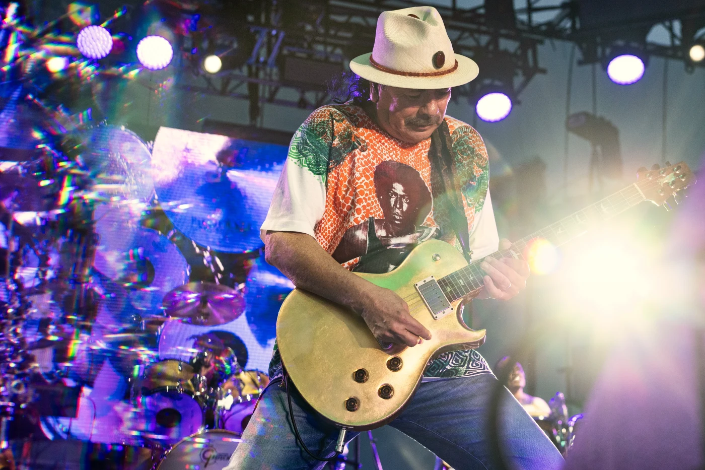 Guitarist in a white hat soloing under purple and blue stage lights