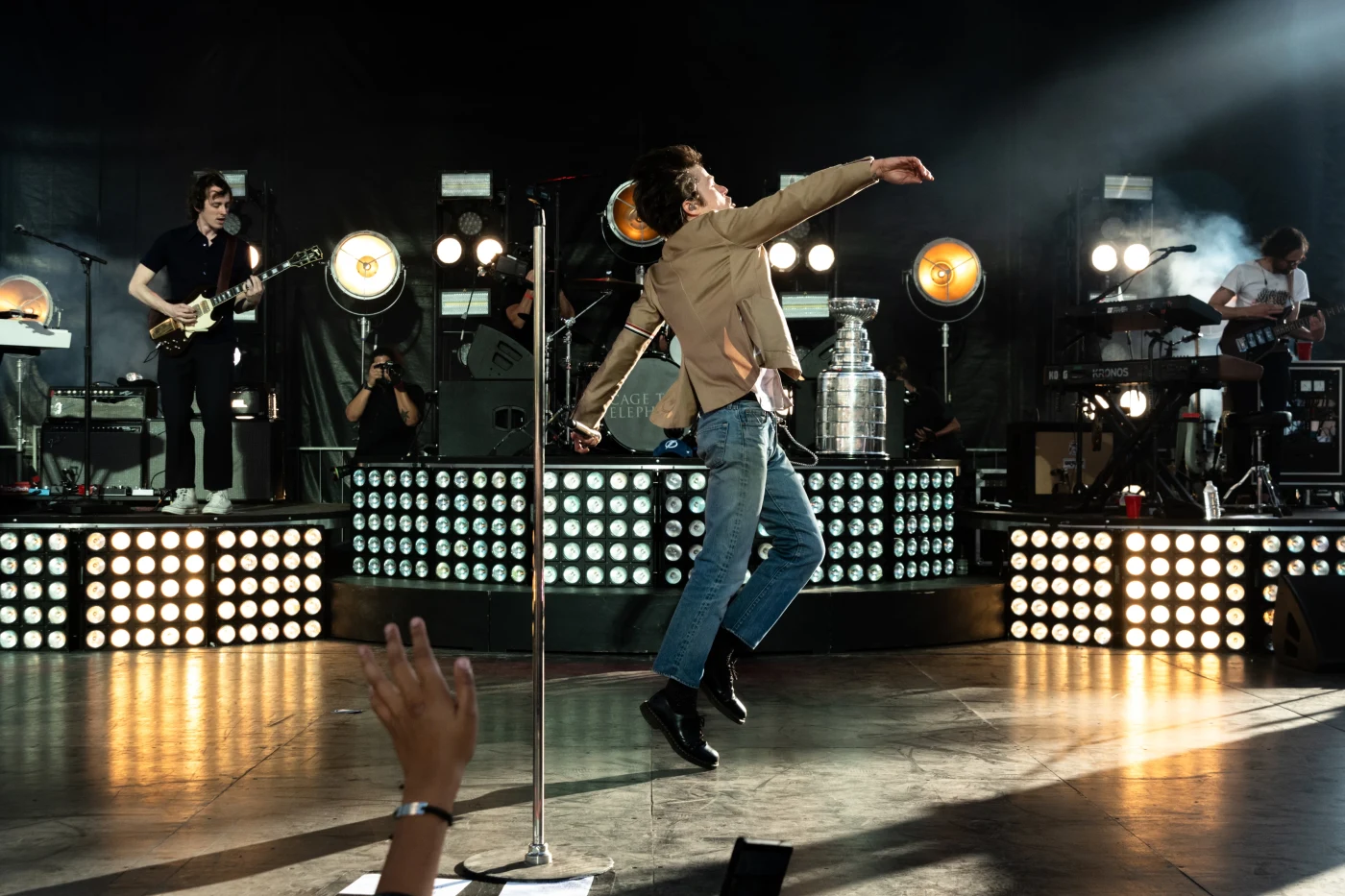 Frontman leaping across the stage in front of light banks